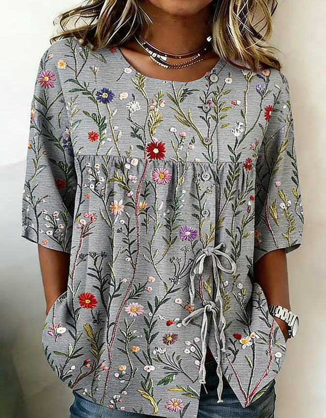 Gray tunic blouse with a colorful wildflower print, button-front detail, drawstring tie, and elbow-length sleeves.