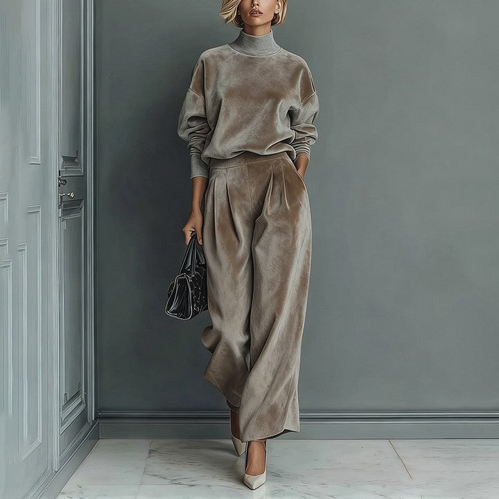 A model wears a taupe velour long-sleeve high-neck top and matching wide-leg pleated trousers with heels and a bag.