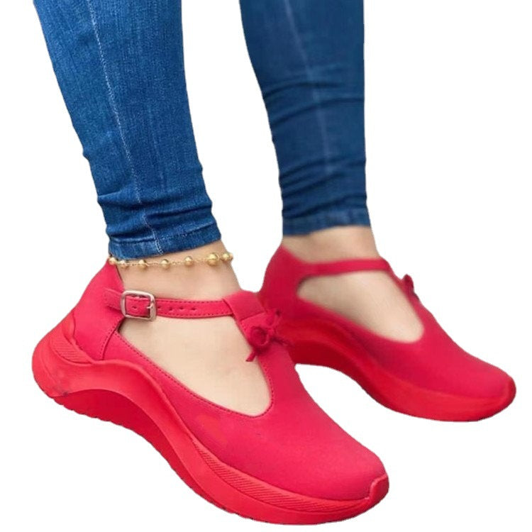 Bright red suede-style platform sneakers with T-strap buckle closures, worn with blue jeans and an anklet.