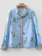 Floral print ruffled V-neck blouse with striped trim, trendy Tops by Trendsi, showcasing the detailed floral design and ruffled neckline.