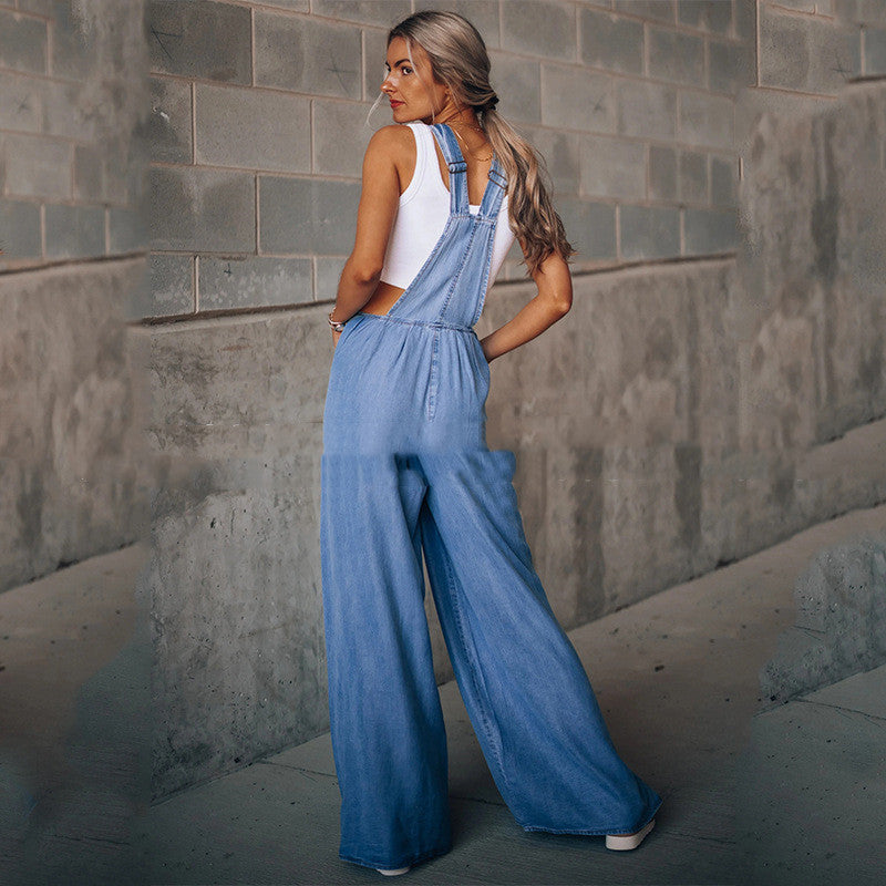 Woman in a white tank top wearing light-wash blue denim overalls with a relaxed, wide-leg fit.