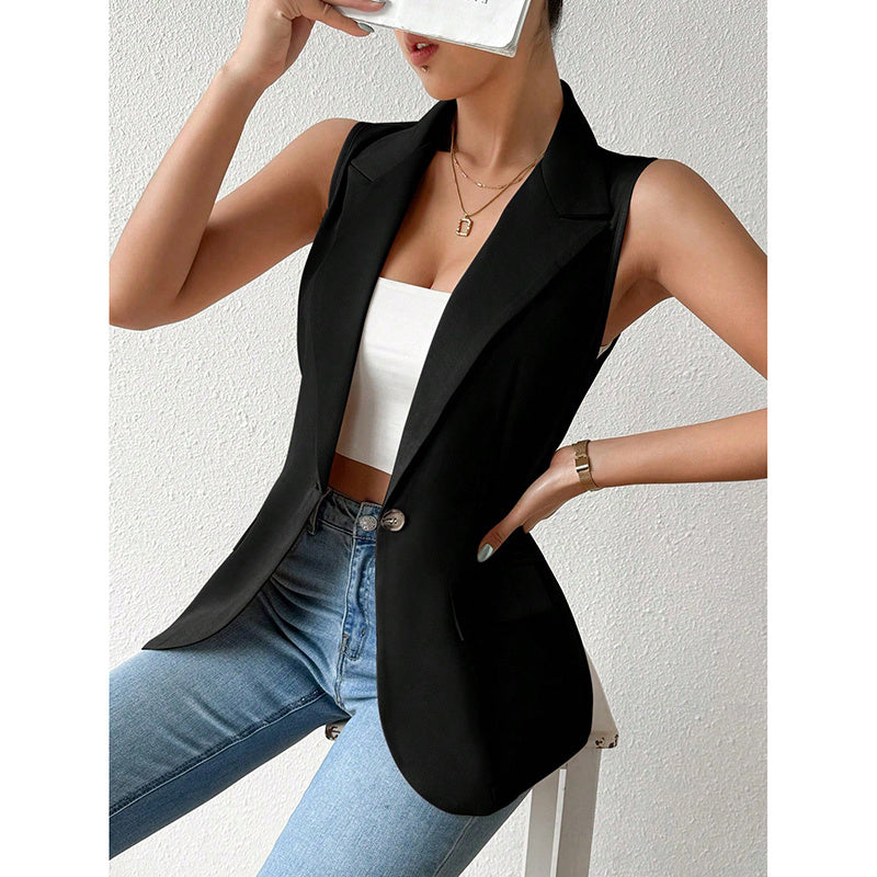 A woman wears a sleeveless, black single-button blazer over a white crop top and blue jeans.