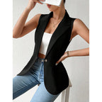 A woman wears a sleeveless, black single-button blazer over a white crop top and blue jeans.