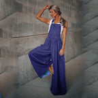 A woman wears loose-fitting deep blue denim overalls with wide legs over a simple white tank top.