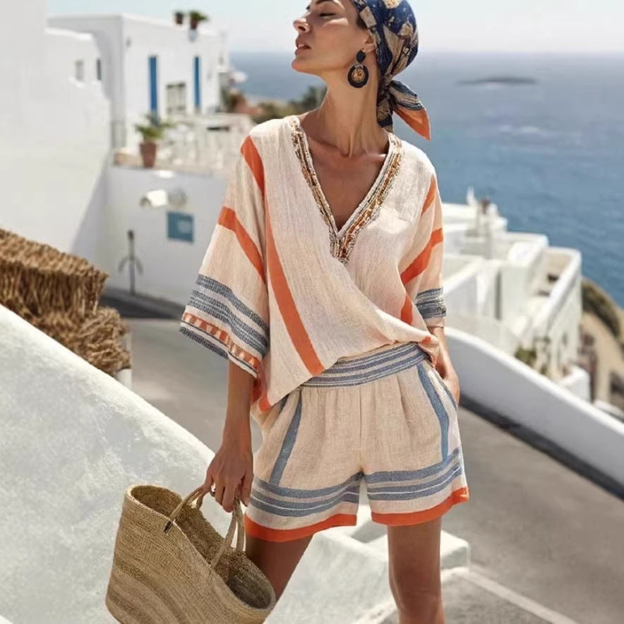 A woman in a beige, orange, and blue striped linen tunic and matching shorts set, styled with a headscarf and bag.