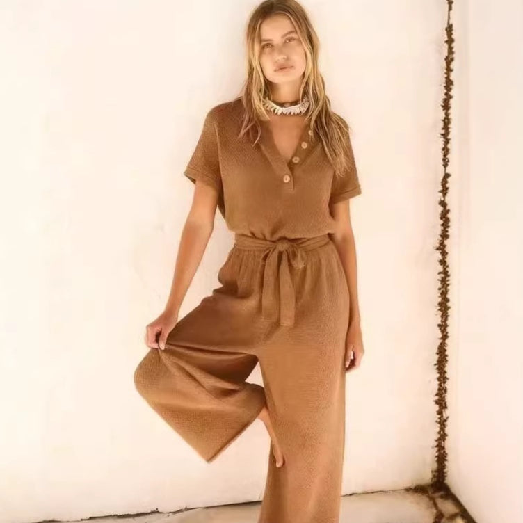 A woman wears a textured, camel-colored knit jumpsuit with a collared, button-down bodice and a tie-waist belt.