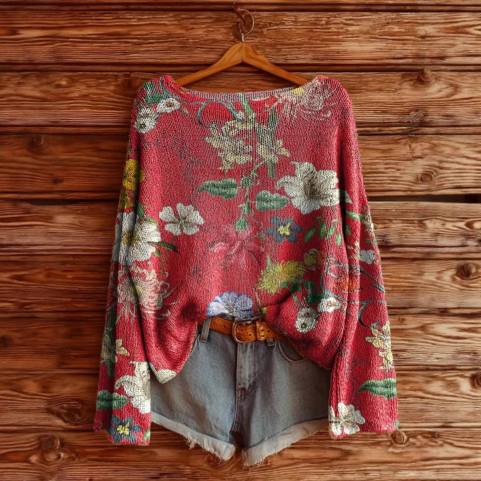 A red, long-sleeve knit sweater with a colorful floral pattern, styled with denim shorts on a wooden background.