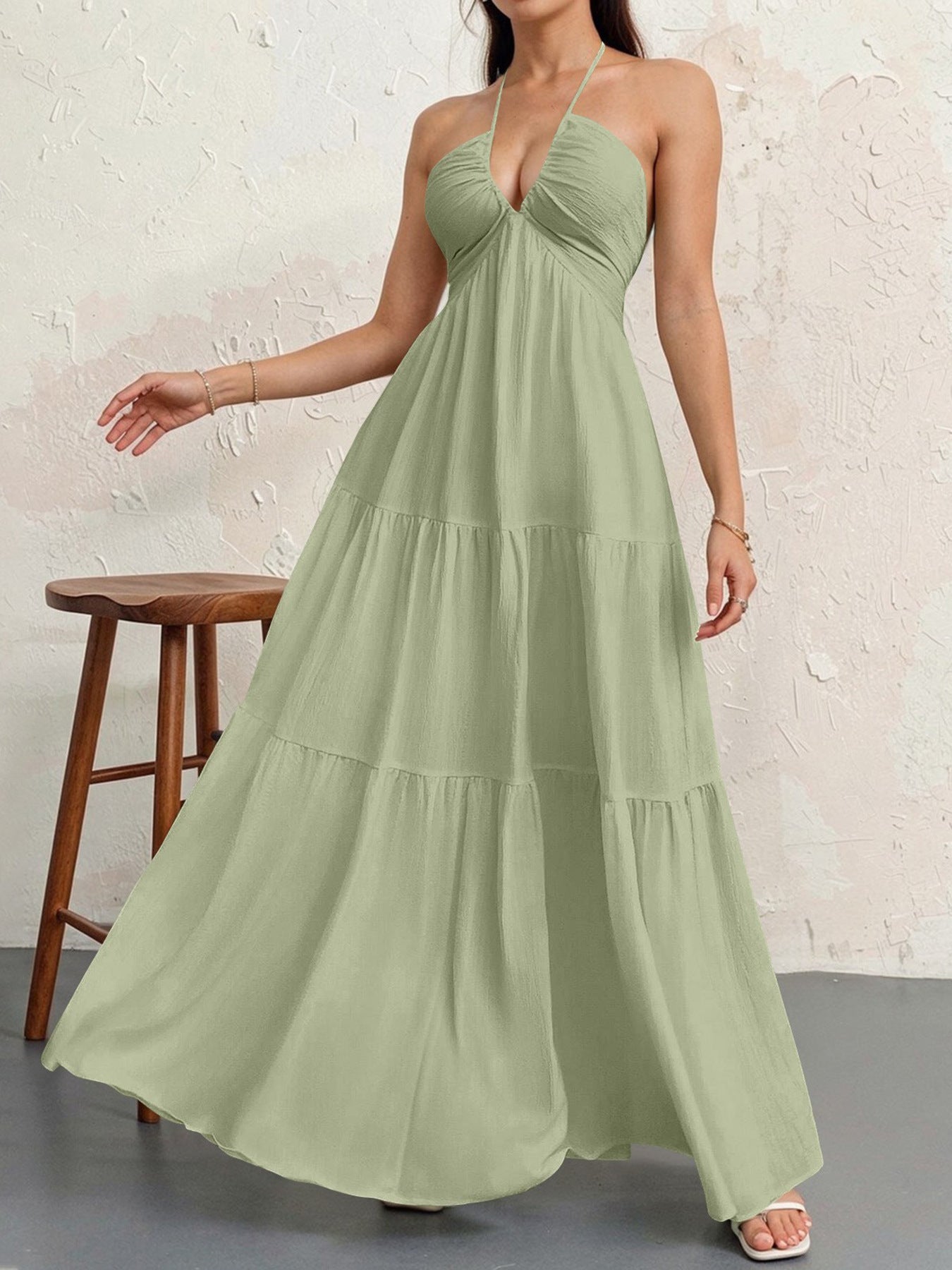 Sage green halter-neck maxi dress with a textured fabric and a tiered, flowing skirt.