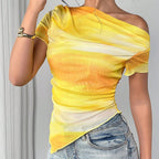 Sheer yellow and orange tie-dye asymmetric top with a draped neckline and short sleeves worn with denim jeans.