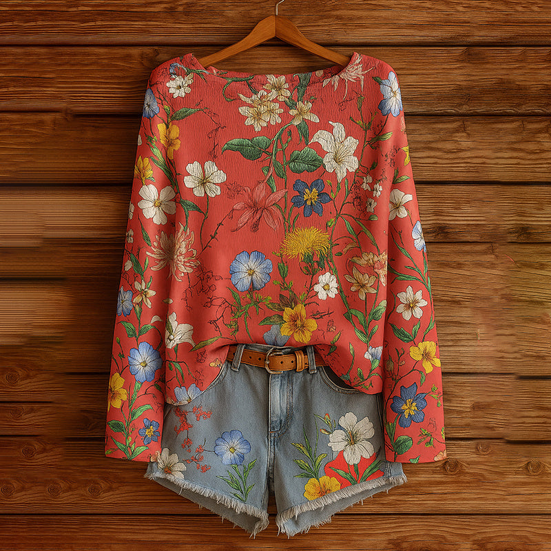 Red long-sleeve blouse with a vibrant, multi-colored floral print and matching raw-hem denim shorts with a brown belt.