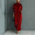 A woman wears a red velour set with a high-neck long-sleeve top and matching high-waisted wide-leg trousers.