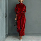 A woman wears a red velour set with a high-neck long-sleeve top and matching high-waisted wide-leg trousers.
