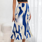 A pleated midi skirt in cream with a bold blue abstract wavy print, worn with a black crop top.