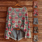 Oversized knit sweater featuring a vintage floral print in shades of pink, green, and cream on a wooden background.