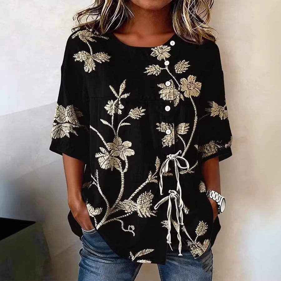 Black blouse with beige floral embroidery, short sleeves, white buttons, and a front drawstring tie detail.