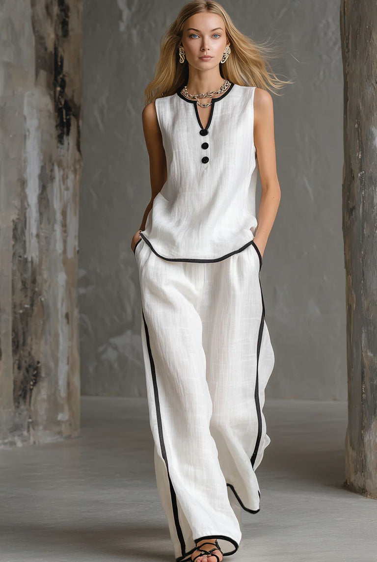 A blonde model wears a white sleeveless linen top and wide-leg trousers with black piping trim and button detail.