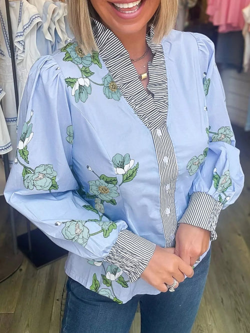 Floral print ruffled V-neck blouse with striped trim, trendy top by Trendsi featuring feminine design and lightweight fabric.