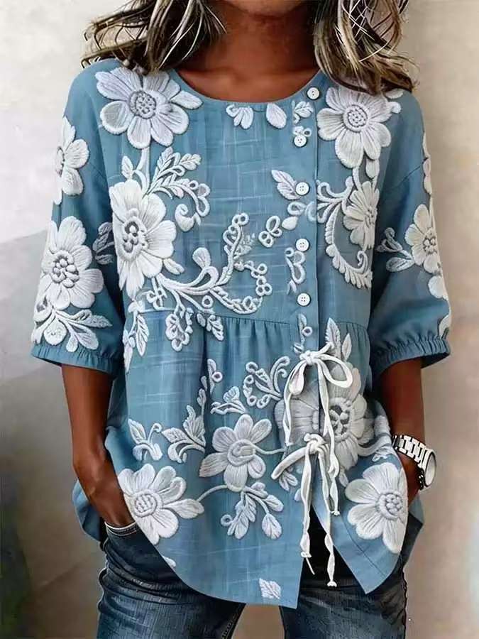 Blue blouse with white floral embroidery, button side closure, gathered waist, and three-quarter length sleeves.