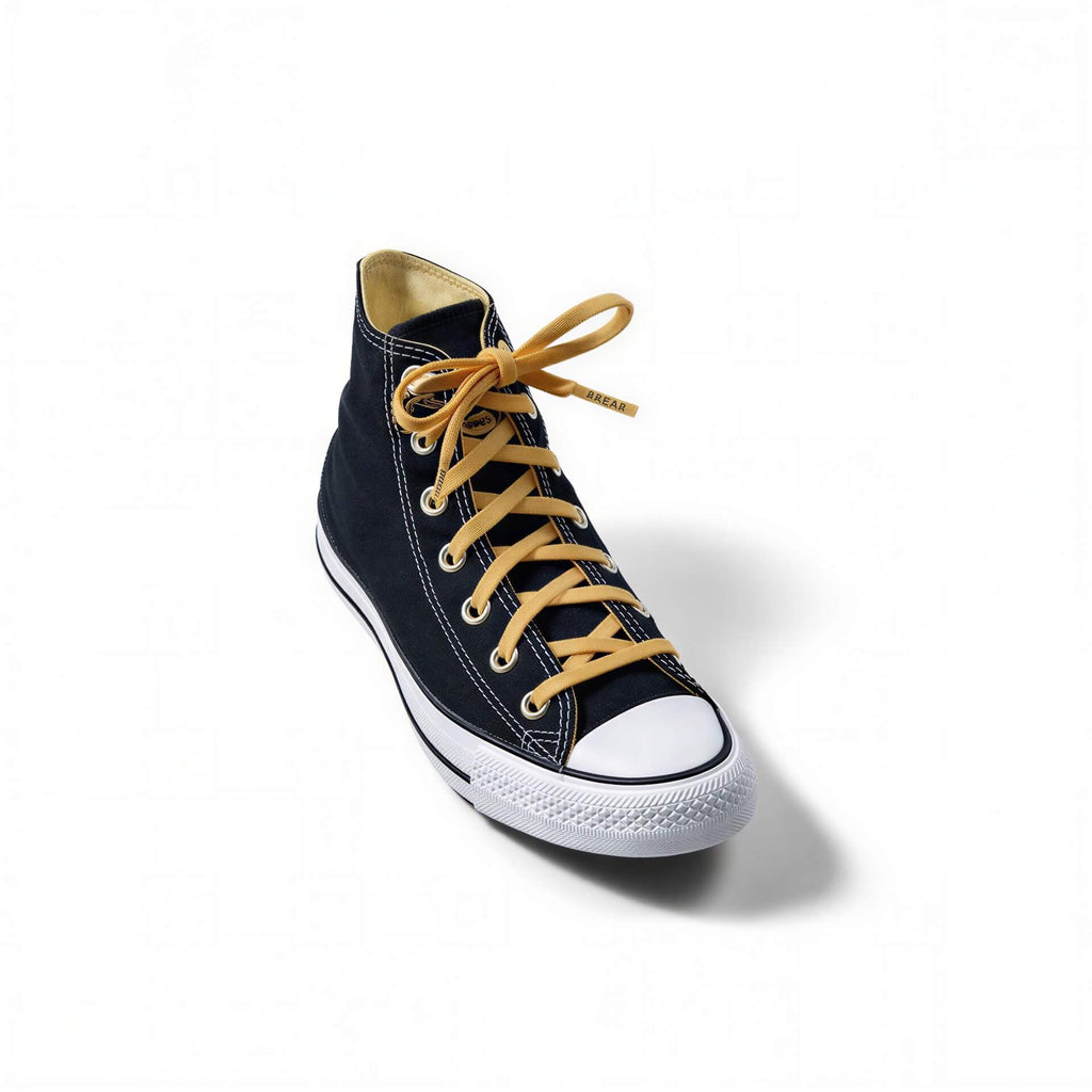Black high-top canvas sneaker with a white rubber toe cap and thick, mustard yellow laces.