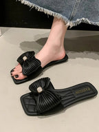 Women's beige faux leather flat sandals with a decorative bow-knot detail, stylish and comfortable for casual wear.