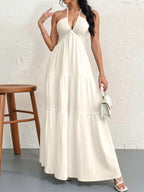 A white tiered maxi dress with a halter neckline, worn with a small white handbag and white strappy sandals.