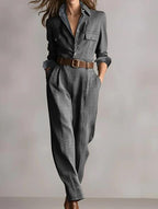 Model wearing a grey plaid jumpsuit with a button-down collar, utility pockets, and a brown leather belt.