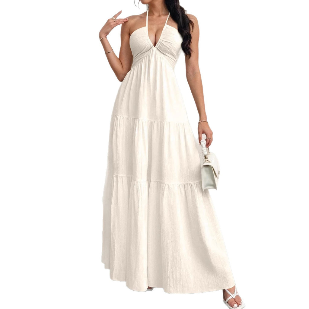 A woman wearing a cream, textured halter-neck maxi dress with a deep V-neck and a tiered, flowing skirt.