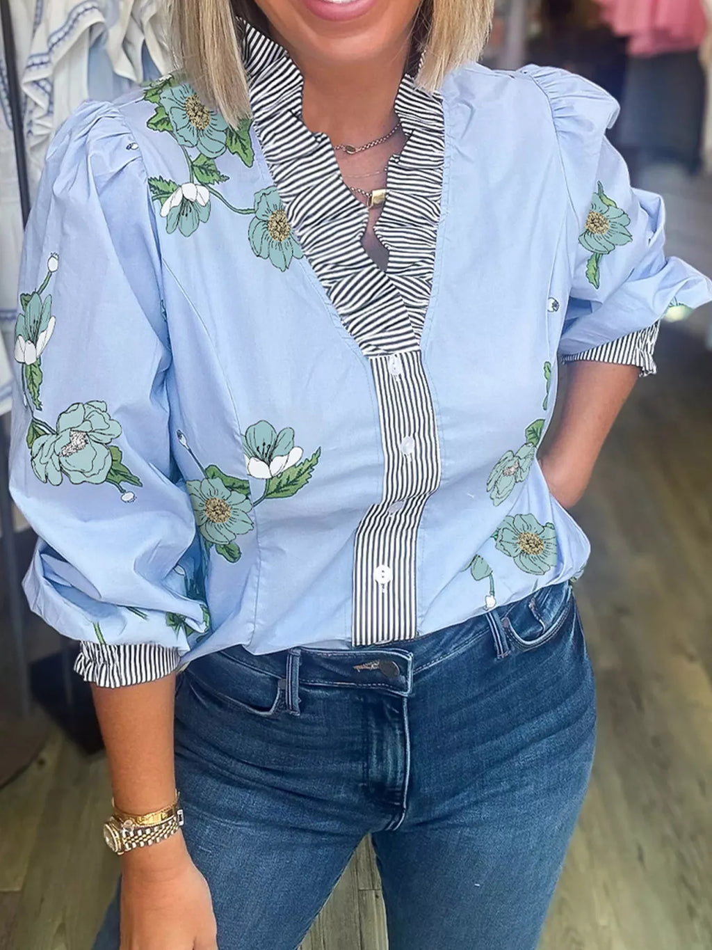 Floral print ruffled v-neck blouse with striped trim, stylish trendy top from Trendsi, shown with ruffled details and vibrant floral pattern.