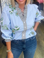 Floral print ruffled v-neck blouse with striped trim, stylish trendy top from Trendsi, shown with ruffled details and vibrant floral pattern.