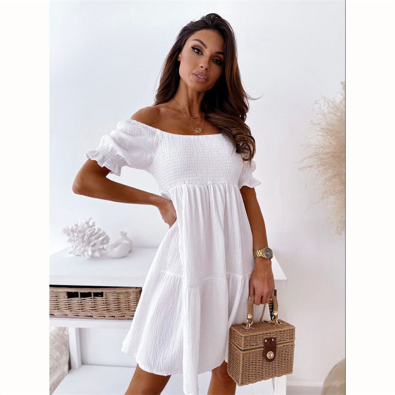 A woman wears a white, off-the-shoulder, smocked mini dress with puff sleeves and carries a woven rattan box bag.